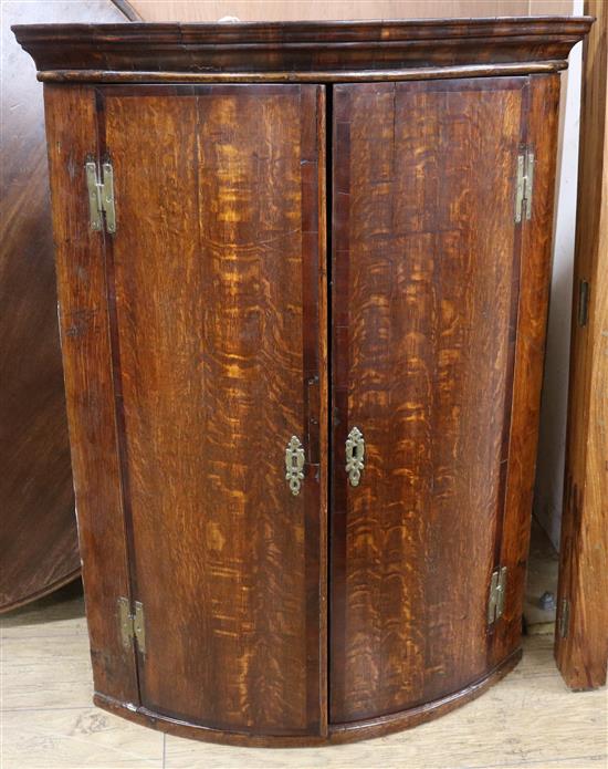 A George III bow front oak hanging corner cupboard W.76cm